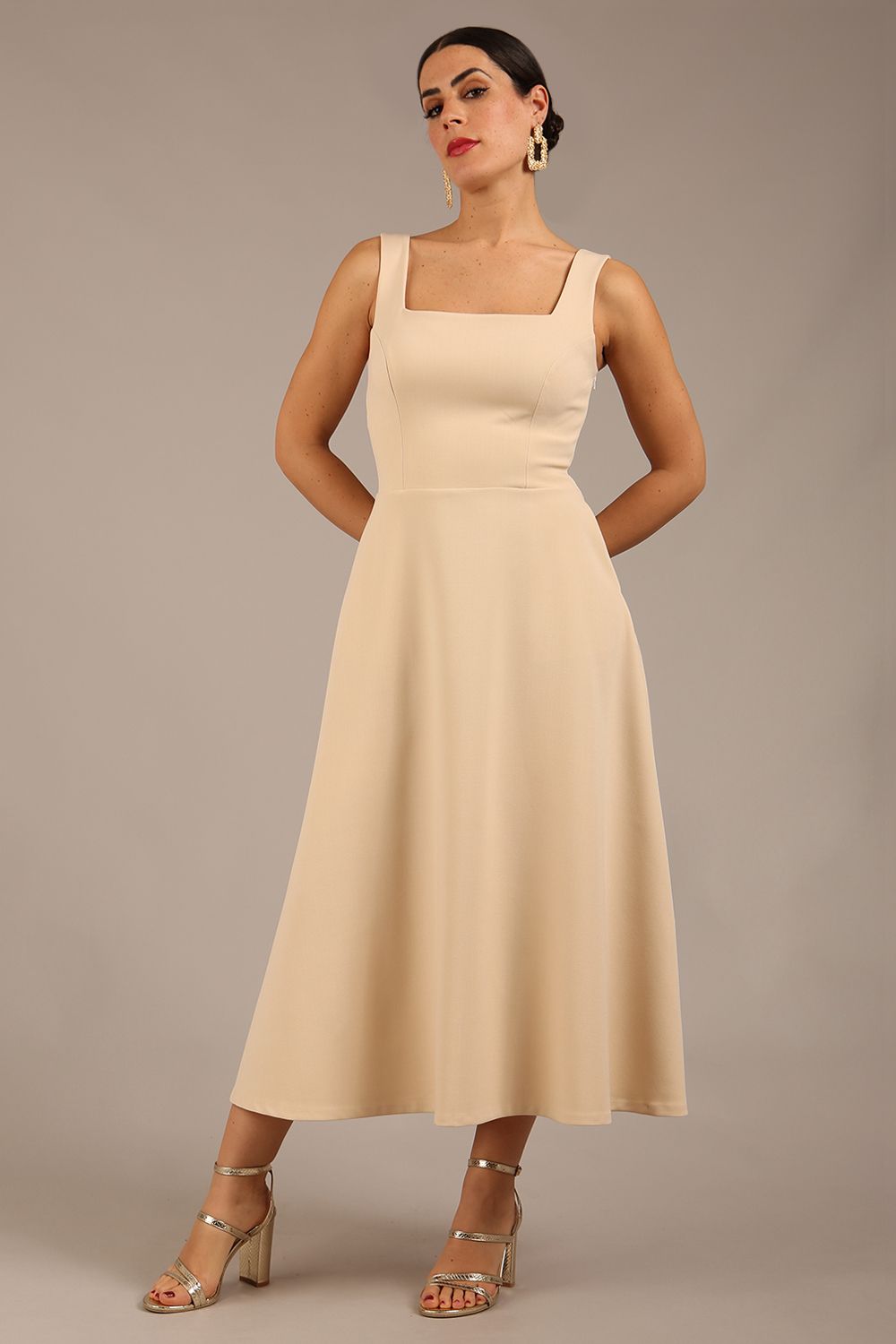 brunette model is wearing a diva catwalk Tamsin Square Neckline Swing Dress sleeveless style with a midaxi  length and side pockets in (Sandshell beige) colour front