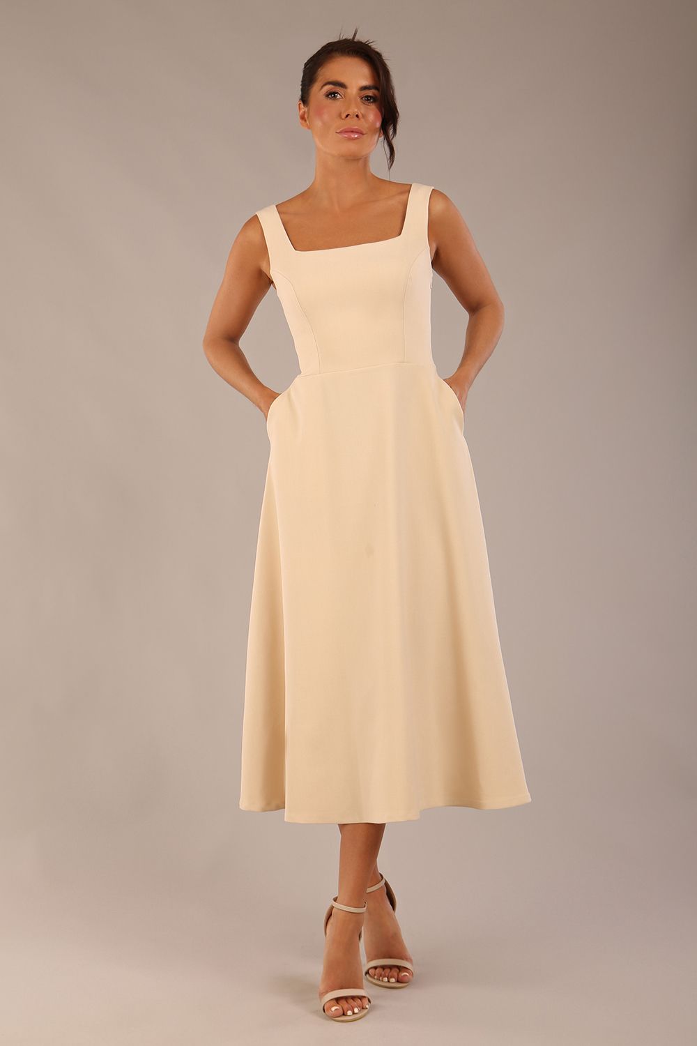 brunette model wearing a diva catwalk Tamsin Square Neckline Swing Dress sleeveless style with a midaxi  length and side pockets in Sandshell Beige colour front