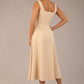 brunette model wearing a diva catwalk Tamsin Square Neckline Swing Dress sleeveless style with a midaxi  length and side pockets in Sandshell Beige colour back