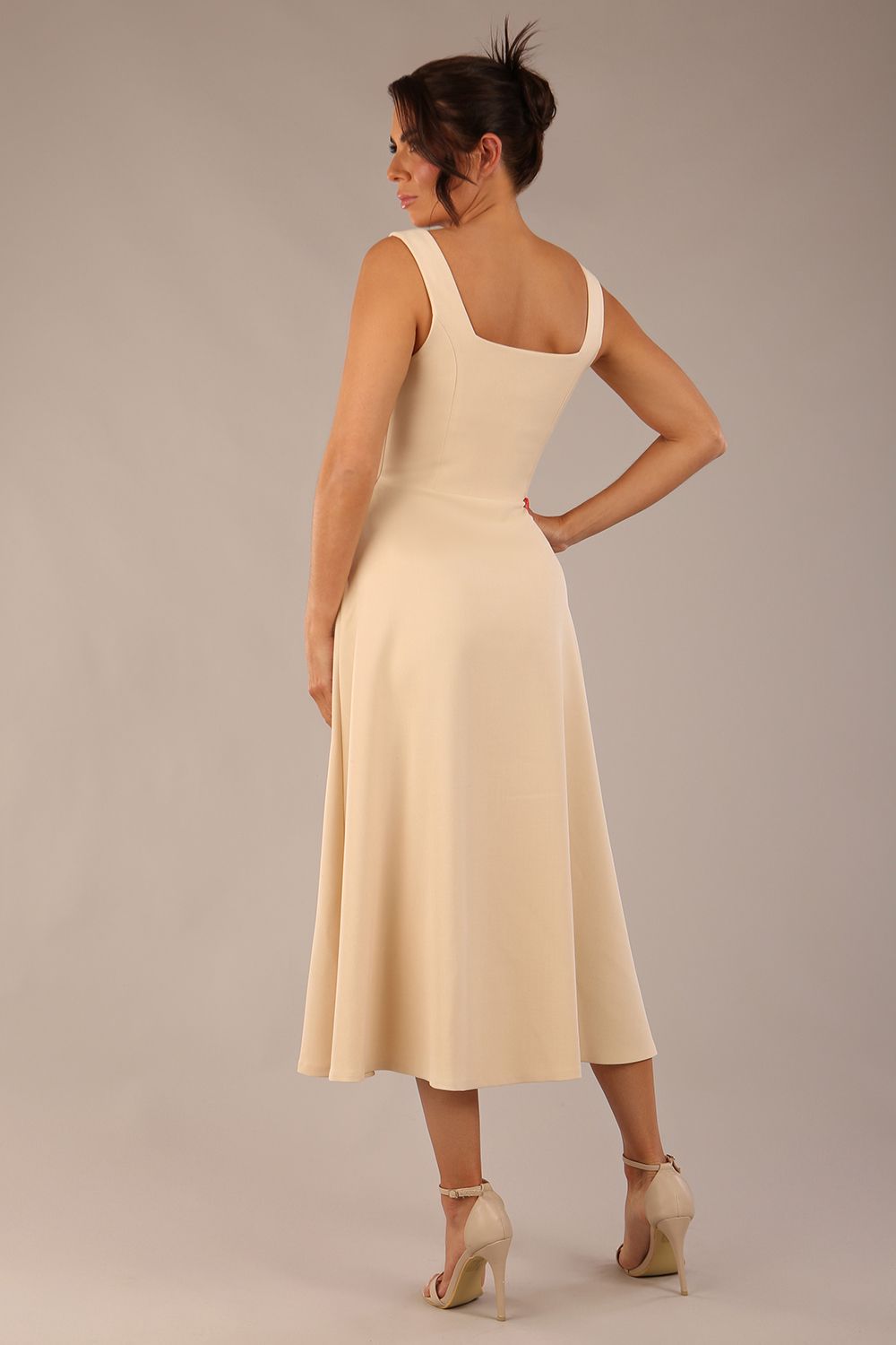 brunette model wearing a diva catwalk Tamsin Square Neckline Swing Dress sleeveless style with a midaxi  length and side pockets in Sandshell Beige colour back