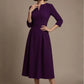 Woman wearing a diva catwalk Amanda Pleated a-line dress in a magenta pink colour against a beige background (Purple)