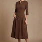 Woman wearing a diva catwalk Amanda Pleated a-line dress in a magenta pink colour against a beige background (Peppercorn Brown)