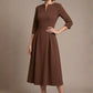 Woman wearing a diva catwalk Amanda Pleated a-line dress in a magenta pink colour against a beige background (Peppercorn Brown)