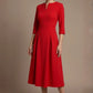 Woman wearing a diva catwalk Amanda Pleated a-line dress in a magenta pink colour against a beige background (Passion Red)
