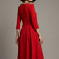 Woman wearing a diva catwalk Amanda Pleated a-line dress in a magenta pink colour against a beige background (Passion Red)