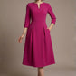 Woman wearing a diva catwalk Amanda Pleated a-line dress in a magenta pink colour with pockets against a beige background (Magenta)