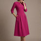 Woman wearing a diva catwalk Amanda Pleated a-line dress in a magenta pink colour with pockets against a beige background (Magenta)