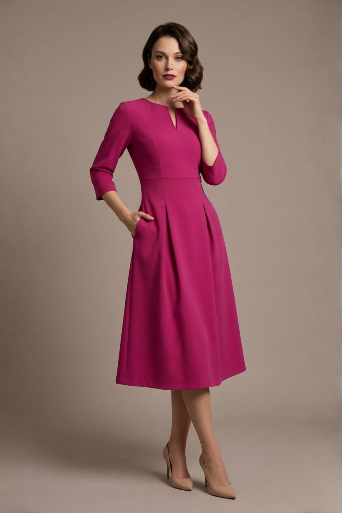 Woman wearing a diva catwalk Amanda Pleated a-line dress in a magenta pink colour with pockets against a beige background (Magenta)