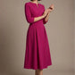 Woman wearing a diva catwalk Amanda Pleated a-line dress in a magenta pink colour against a beige background (Magenta)