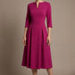 Woman wearing a diva catwalk Amanda Pleated a-line dress in a magenta pink colour against a beige background (Magenta)