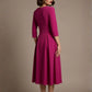 Woman wearing a diva catwalk Amanda Pleated a-line dress in a magenta pink colour against a beige background (Magenta)