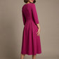 Woman wearing a diva catwalk Amanda Pleated a-line dress in a magenta pink colour against a beige background (Magenta)