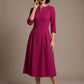 Woman wearing a diva catwalk Amanda Pleated a-line dress in a magenta pink colour against a beige background (Magenta)